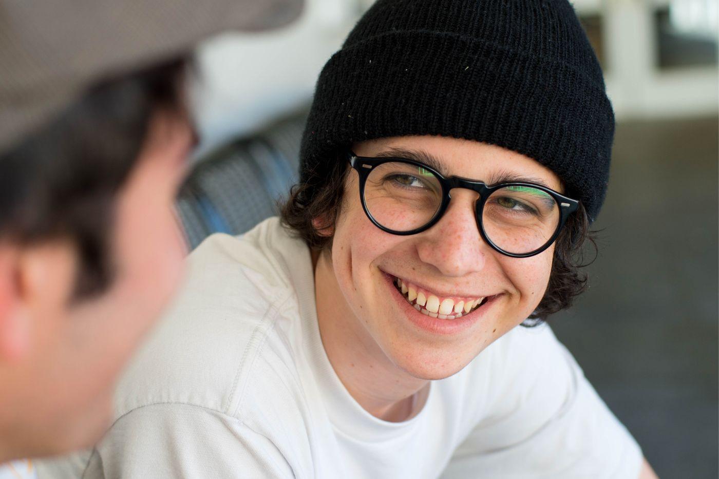 Young man in glasses and hat smiling 